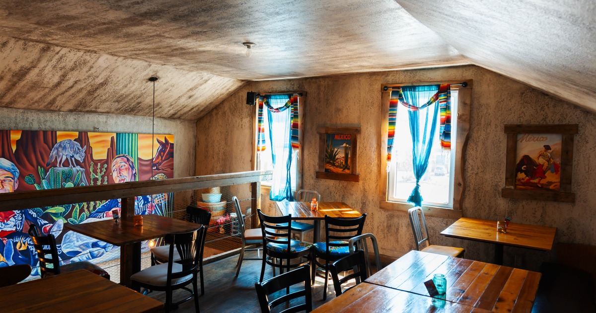 Rustic dining room with wooden tables, mismatched chairs, blue curtains