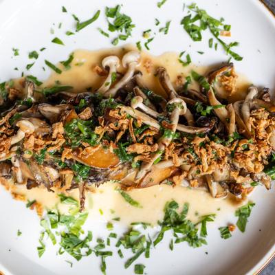 Sauteed mushrooms on white plate with light-brown sauce and fresh herbs
