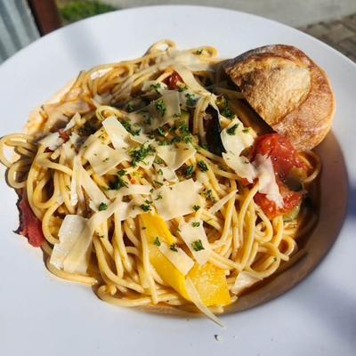 Pasta with vegetables, shaved Parmesan, and a piece of bread.
