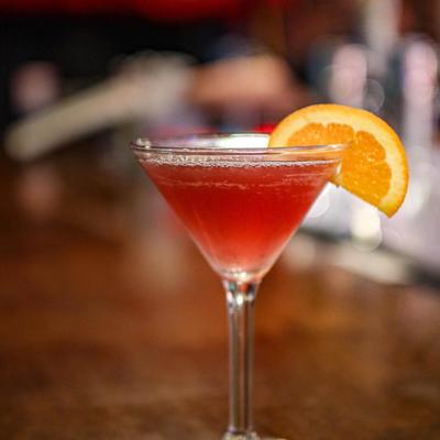 Red cocktail served in martini glass garnished with an orange slice.