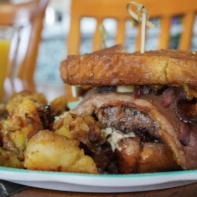 A close-up of a bacon burger with melted cheese, served with breakfast potatoes.
