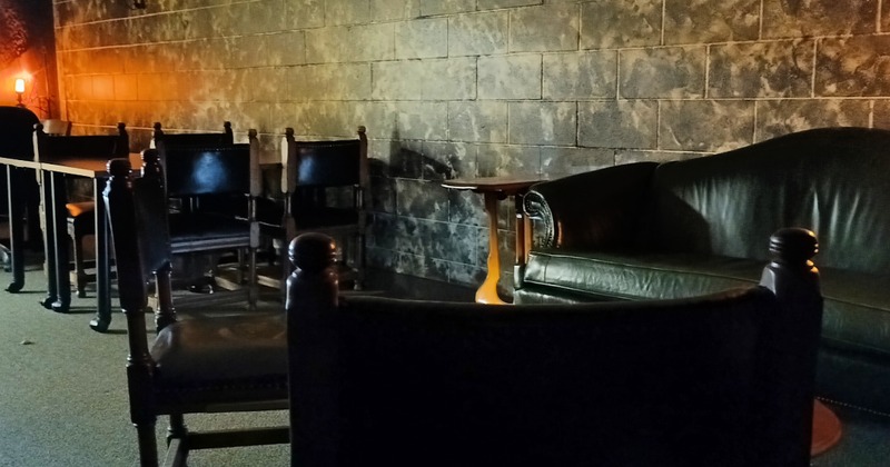 A decorated brick basement spread out with a couch, along with some seats and tables, illuminated by atmospheric lighting.