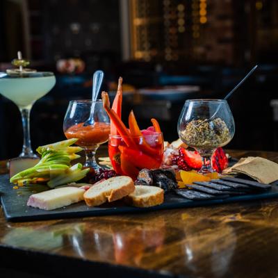 Charcuterie board with vegetables cheese and bread on a slate, accompanied by cocktails.