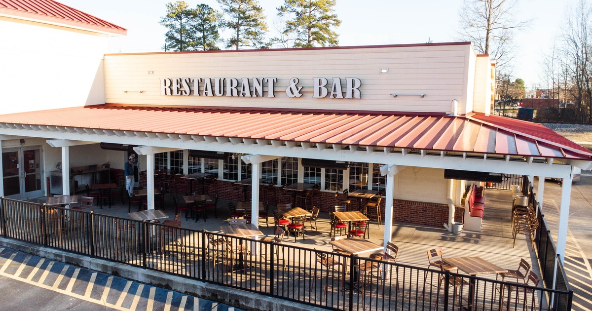 Outdoor patio, metal roof, and black railing with tables and chairs