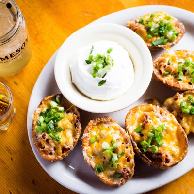 Potato skins topped with cheese and green onion plated with a side of sour cream