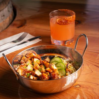 Chicken rice bowl with cucumbers and sauce beside a cocktail.