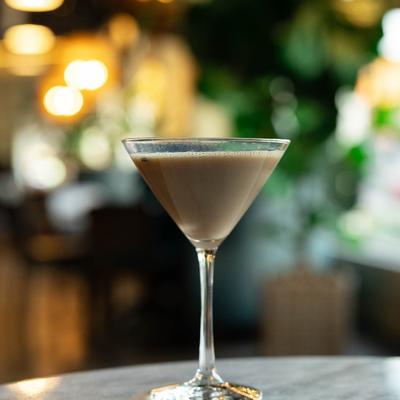 Espresso Martini on a marble table, blurred warm lights and greenery in the background.