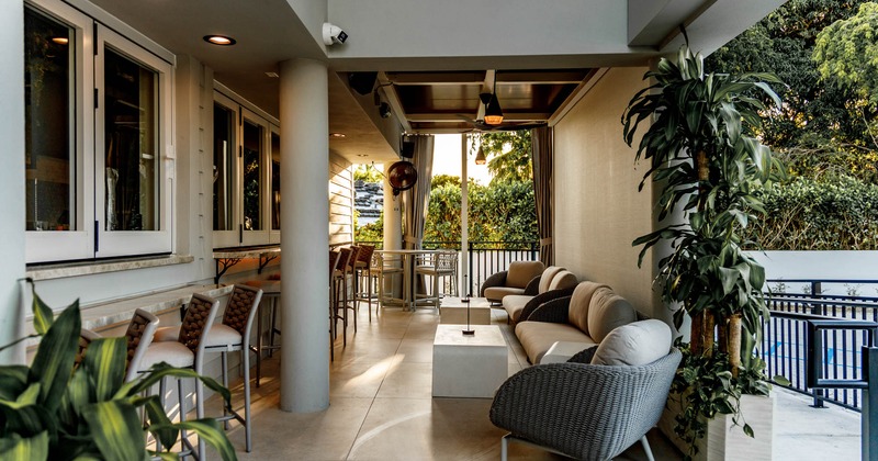 A contemporary patio with cushioned seating, bar stools, and large plants