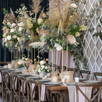 Elegant dining table set for an event, featuring tall, lush floral arrangements
