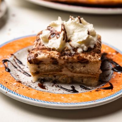 Tiramisu topped with whipped cream and chocolate sauce.