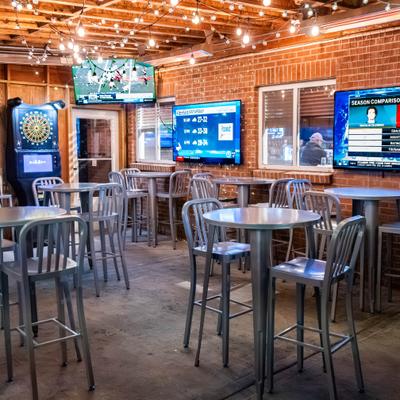 Interior, high top tables and metal bar stools, multiple TVs on a brick walls, string lights.