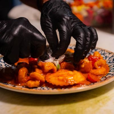 Hands in black gloves plating a pasta dish.