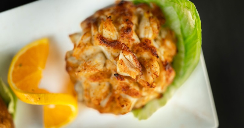 A browned crab cake sits on lettuce with a sliced orange garnish