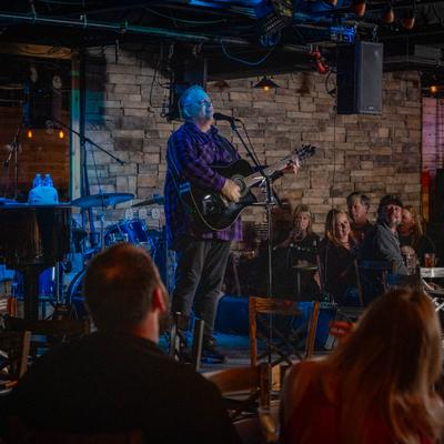 A musician is playing the guitar and singing in front of audience.