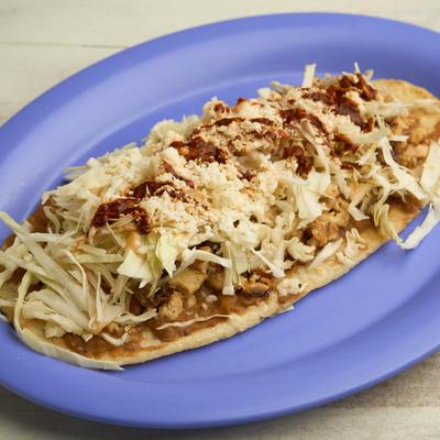 Crispy corn tortilla topped with beans, cheese, cabbage, red salsa, and chicken.