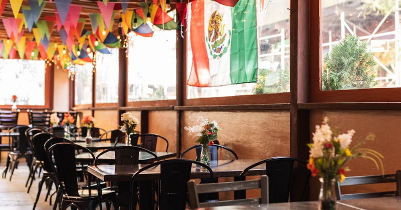 Interior, tables and chairs, Mexican flag hanged on the window, flower vases as centerpieces