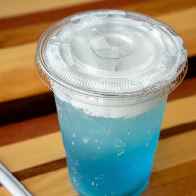Tropical Breeze dirty soda in a clear plastic cup, topped with half and half.