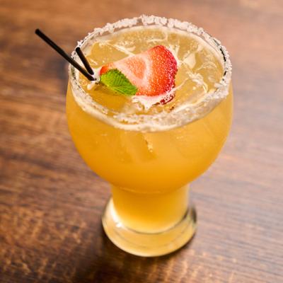 Yellow cocktail in a salt-rimmed glass with strawberry garnish.