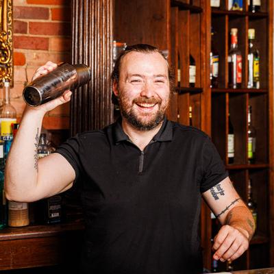 A cheerful bartender shakes a cocktail shaker behind a bar.