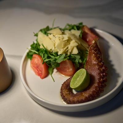 Octopus tentacle served alongside a fresh salad and a half of lime.