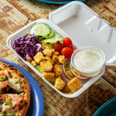 Salad with purple cabbage, croutons, cucumbers, and tomatoes in a foam container.