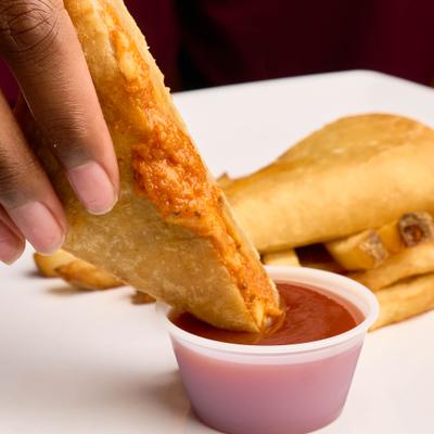 Hand dipping pizza puff into a small container of sauce.