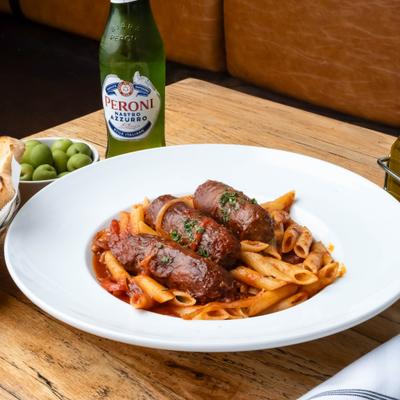 Penne pasta in tomato sauce topped with sausages and served with a bottle of beer.