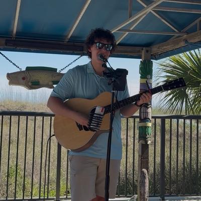 Person playing a guitar under a covered patio.
