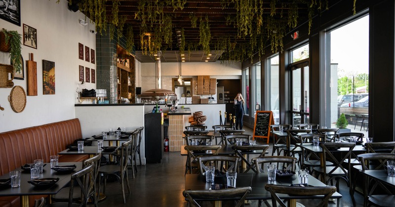 Interior - tables set for dining, hanging greenery , artwork on the walls, large windows