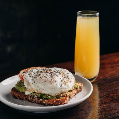 Avocado toast topped with a poached egg, accompanied by orange mimosa drink.