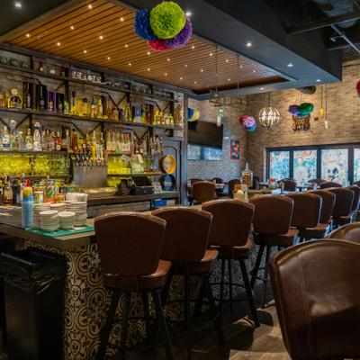 Bar area with brown stools, hanging lights, and shelves of liquor bottles.