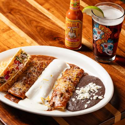 Enchilada Platter with a bottle of hot sauce and a glass of beer on a table.