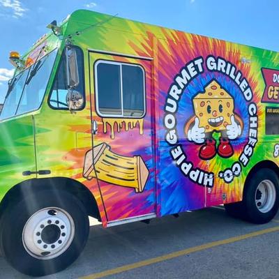 Colorful food truck with a sign featuring cartoon cheese mascot.