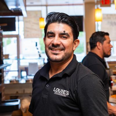 A smiling pizzeria employee in a black Louie’s Pizzeria shirt.