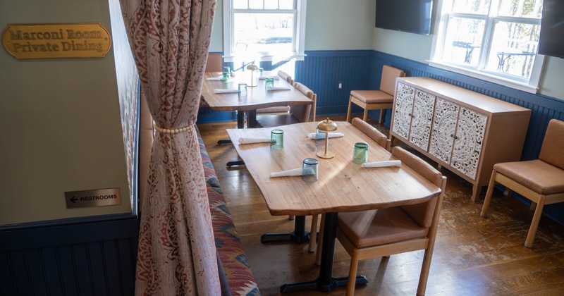 Small private dining room with wooden tables, tan leather chairs, patterned curtain, and large windows