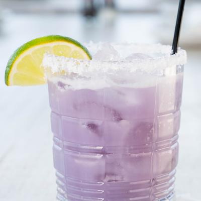 An icy, lavender-colored cocktail with a salted rim and fresh lime wedge.