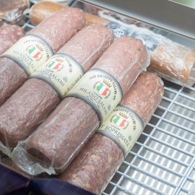 Various cured meats, including Milano salami, in a display cooler.