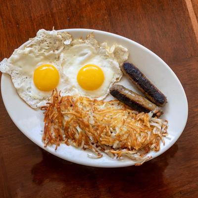 A plate on a wooden table with two sunny-side-up eggs, sausages, and hash browns.