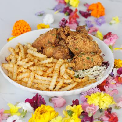 Fried chicken served with crinkle cut fries and coleslaw on a table with colorful dried flowers.