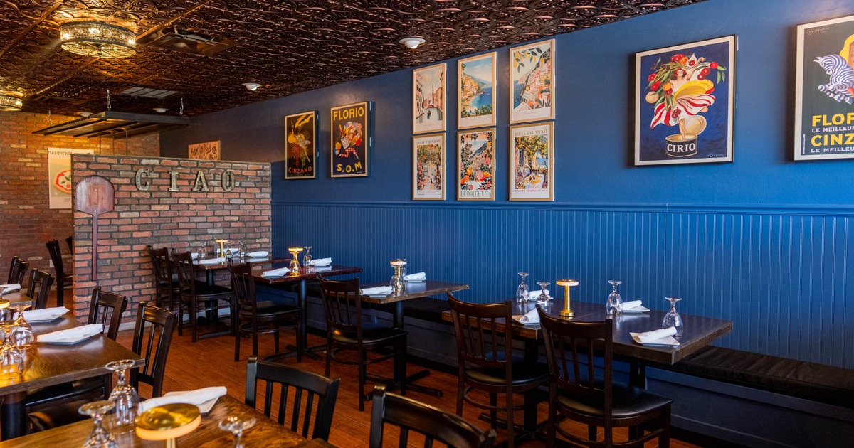 Interior - blue walls with vintage framed posters, brick partition labeled CIAO; neatly set tables