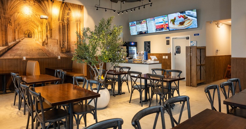Interior - wooden tables, metal chairs, a large mural of a cloister; counter with digital menus