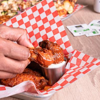 A hand dipping a saucy chicken wing into a cup of ranch.