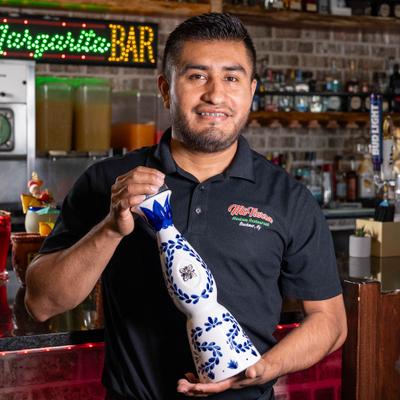 Bartender holding a tequila in blue-and-white ceramic bottle.