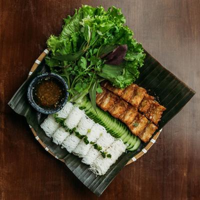 Vietnamese meal with fresh herbs, fried fish, rice noodles, and dipping sauce.