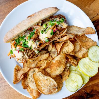 Braised pulled pork sandwich with a side of chips.