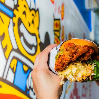 Hands holding Chicken Burger with wall mural in the background.