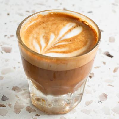 A small glass of cortado, served on a light speckled countertop.