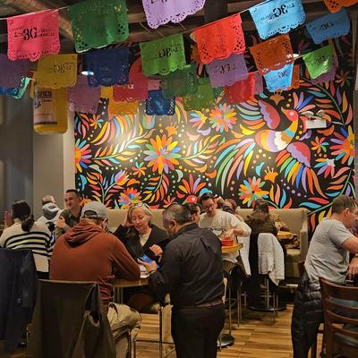 People dining in a restaurant with vibrant wall art and papel picado banners.