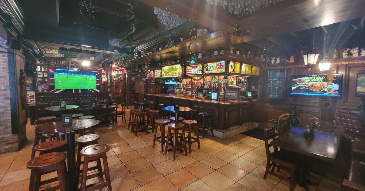 Dark wood interior with a long bar, several high-top tables with wooden stools, and TVs
