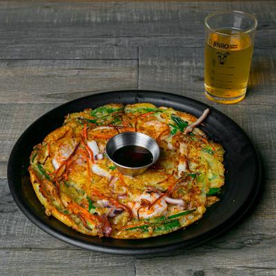 Seafood pancake with a small serving of dipping sauce and a glass of beer.